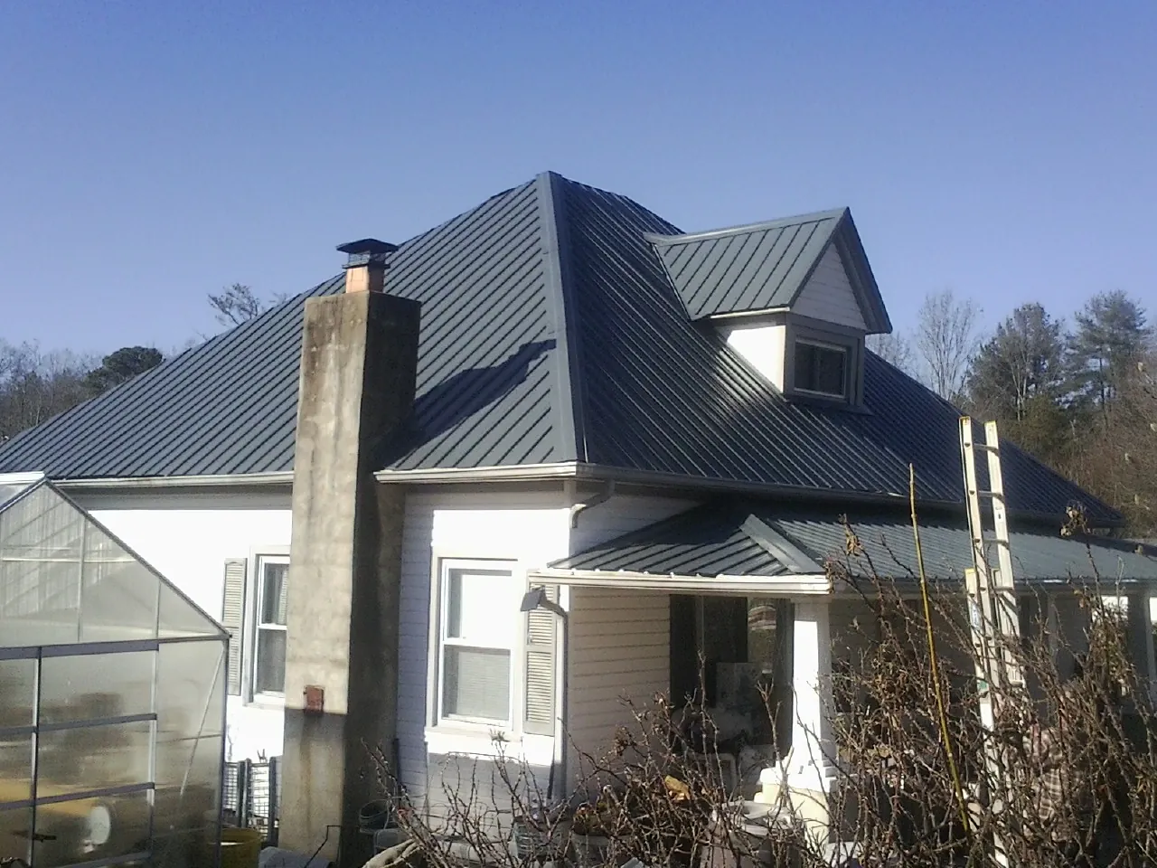 Dark blue standing seam metal roof on a white farmhouse with dormer — Slate & Tile Roof Repair by Roofing Brothers in Superior