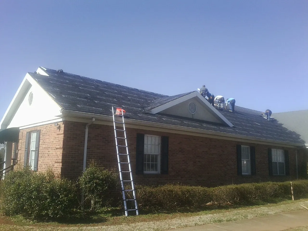 Crew tearing shingles off a brick ranch roof with a ladder set — Emergency Roof Repair work by our crew in Superior