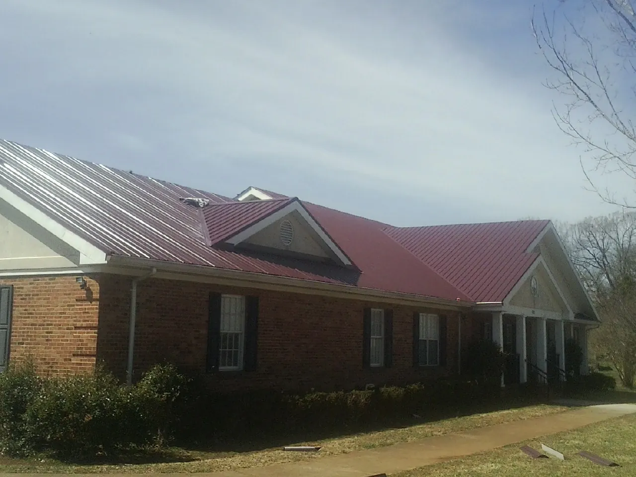 Red metal roof with gabled entries on a long brick building, from a Hail Damage Roof Repair job in Superior