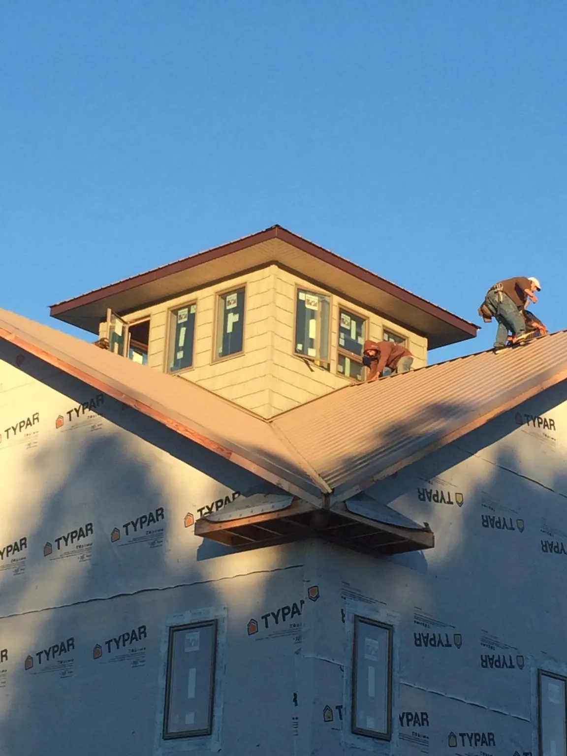 Roofers working around a rooftop cupola on a new metal roof at sunset — Roof Waterproofing in Superior by Roofing Brothers